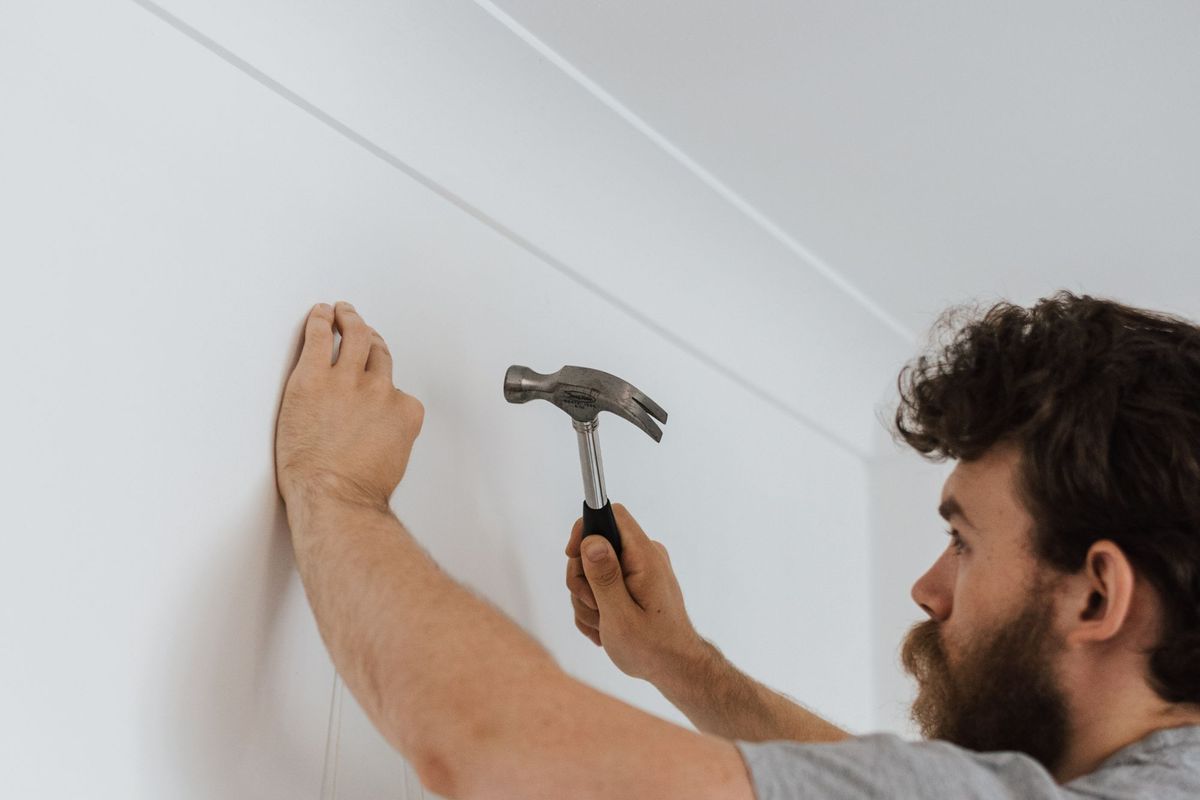 A man hammering a nail into a wall to hang decor