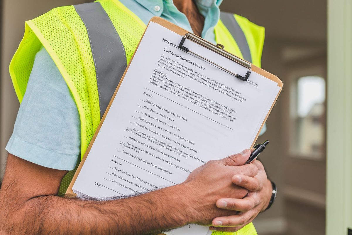 Person in a yellow safety vest holding a clipboard with a house inspection checklist