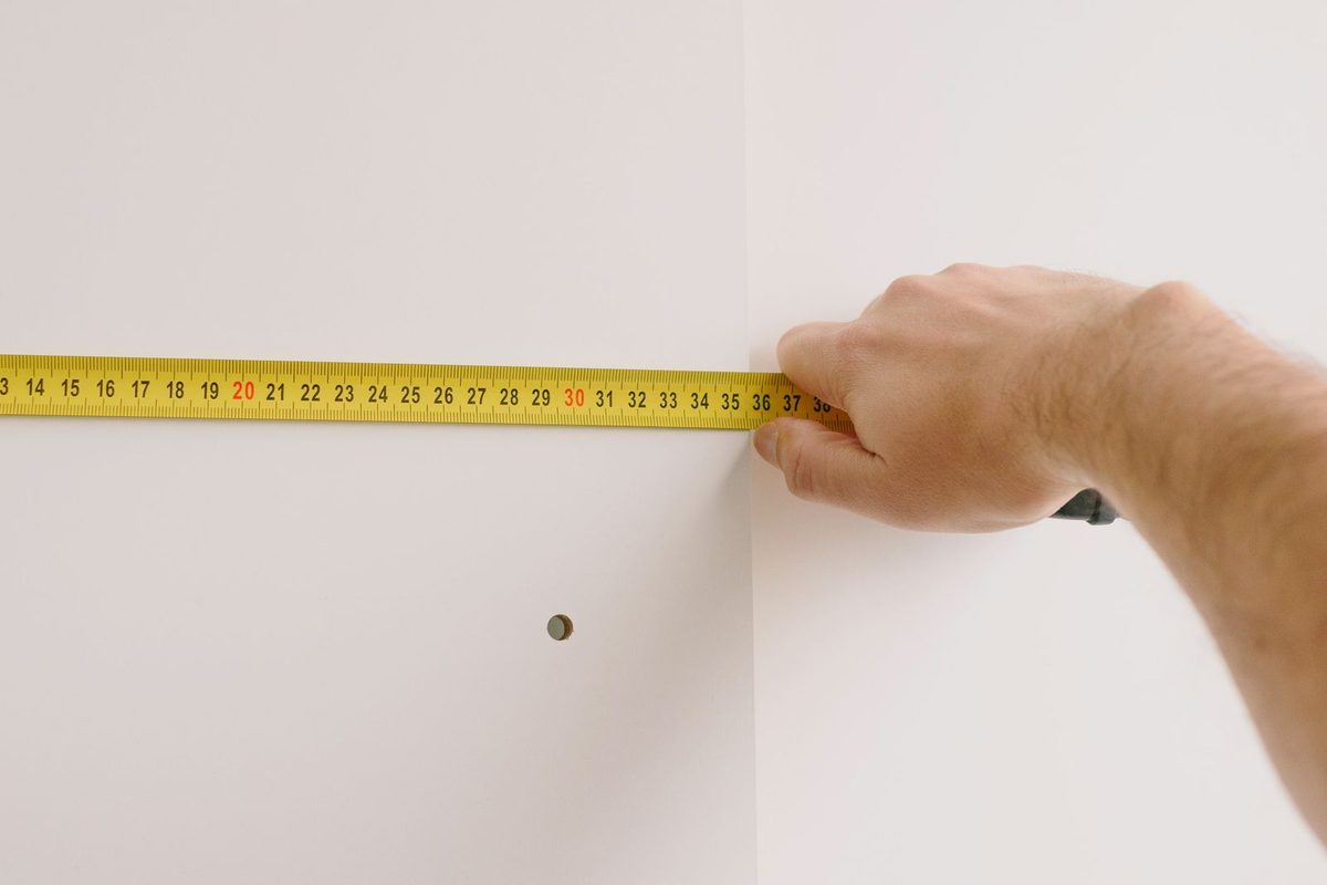 A worker holding a tape measure across a plain white interior wall