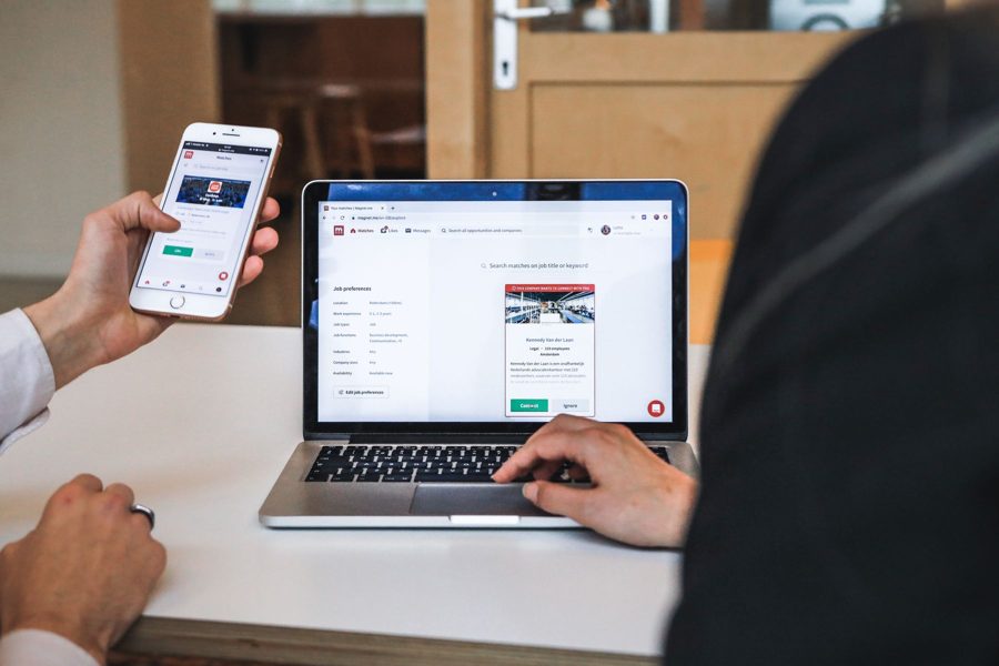 Hands holding a phone next to a laptop showing a search page