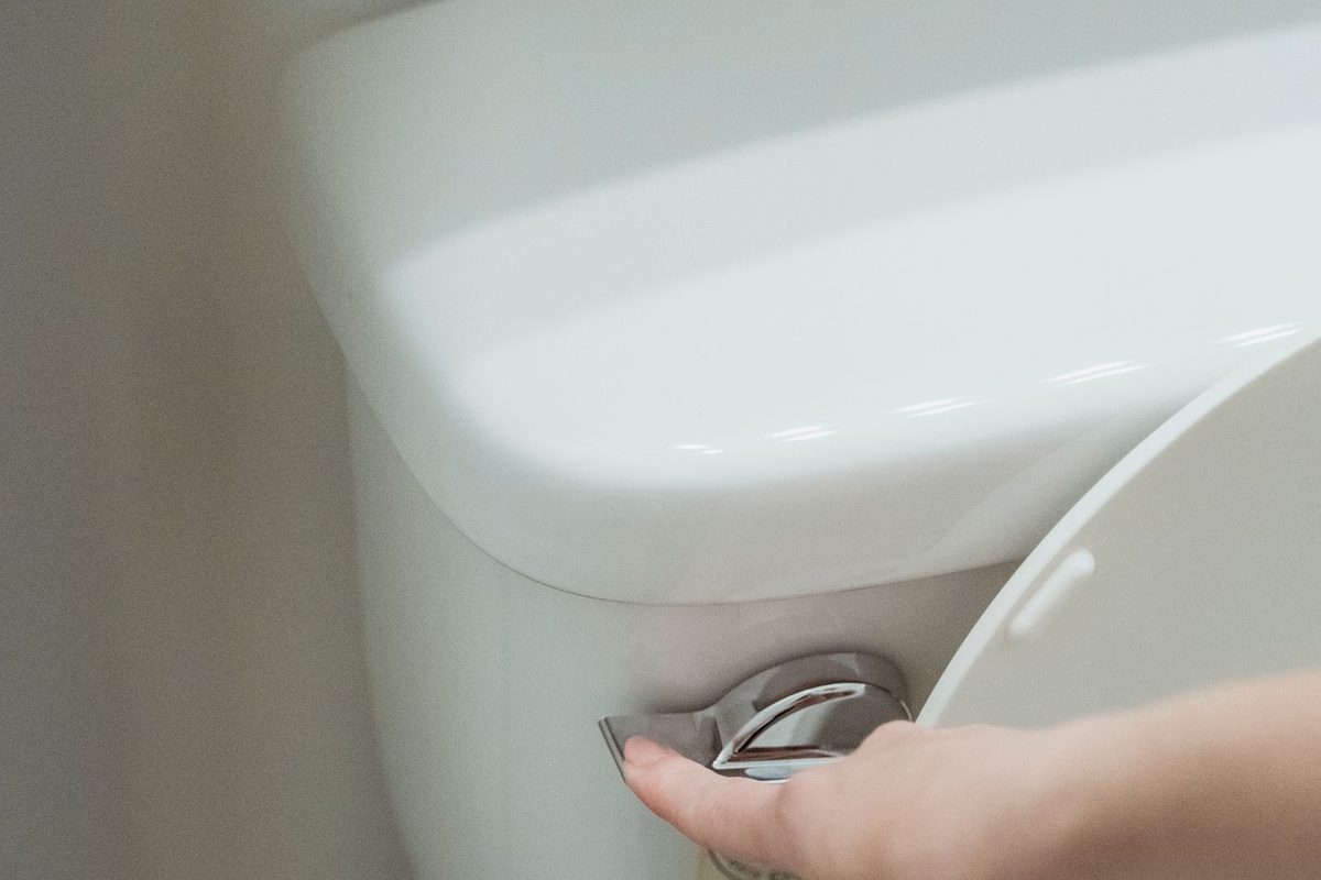 Hand pressing the flush handle on a white toilet tank