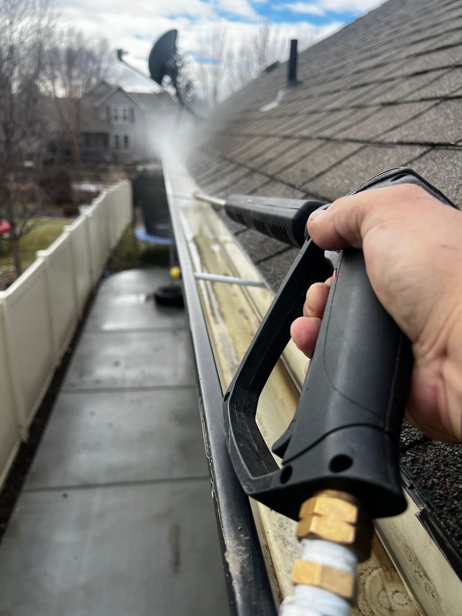 Close view of a rain gutter along a roof edge being cleaned out with a spray wand