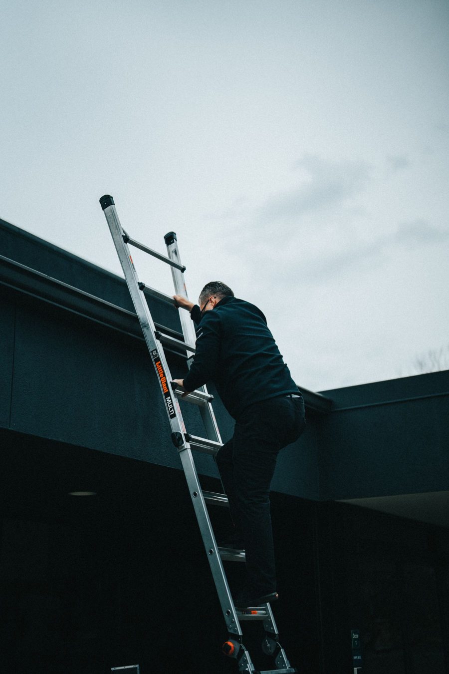Man climbing an aluminum extension ladder leaned against a house at the roof edge