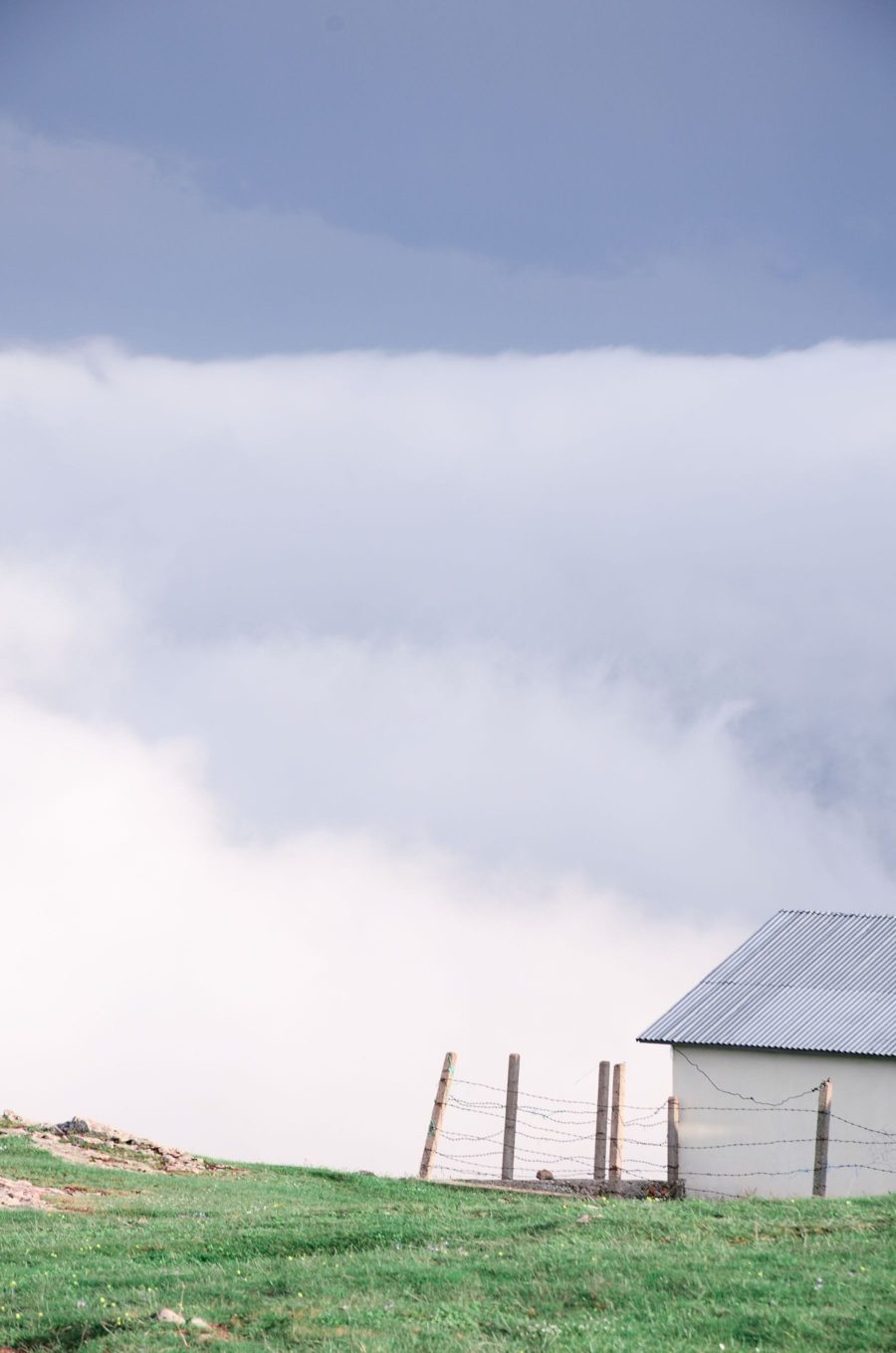 Storm clouds passing over a small building with a metal roof beside a fenced field