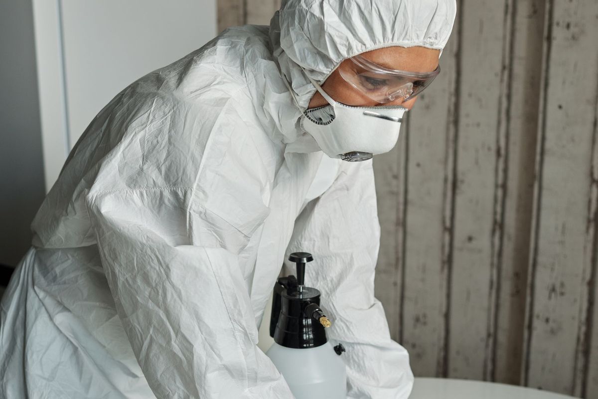 Person in a white protective suit, safety glasses, respirator mask and gloves