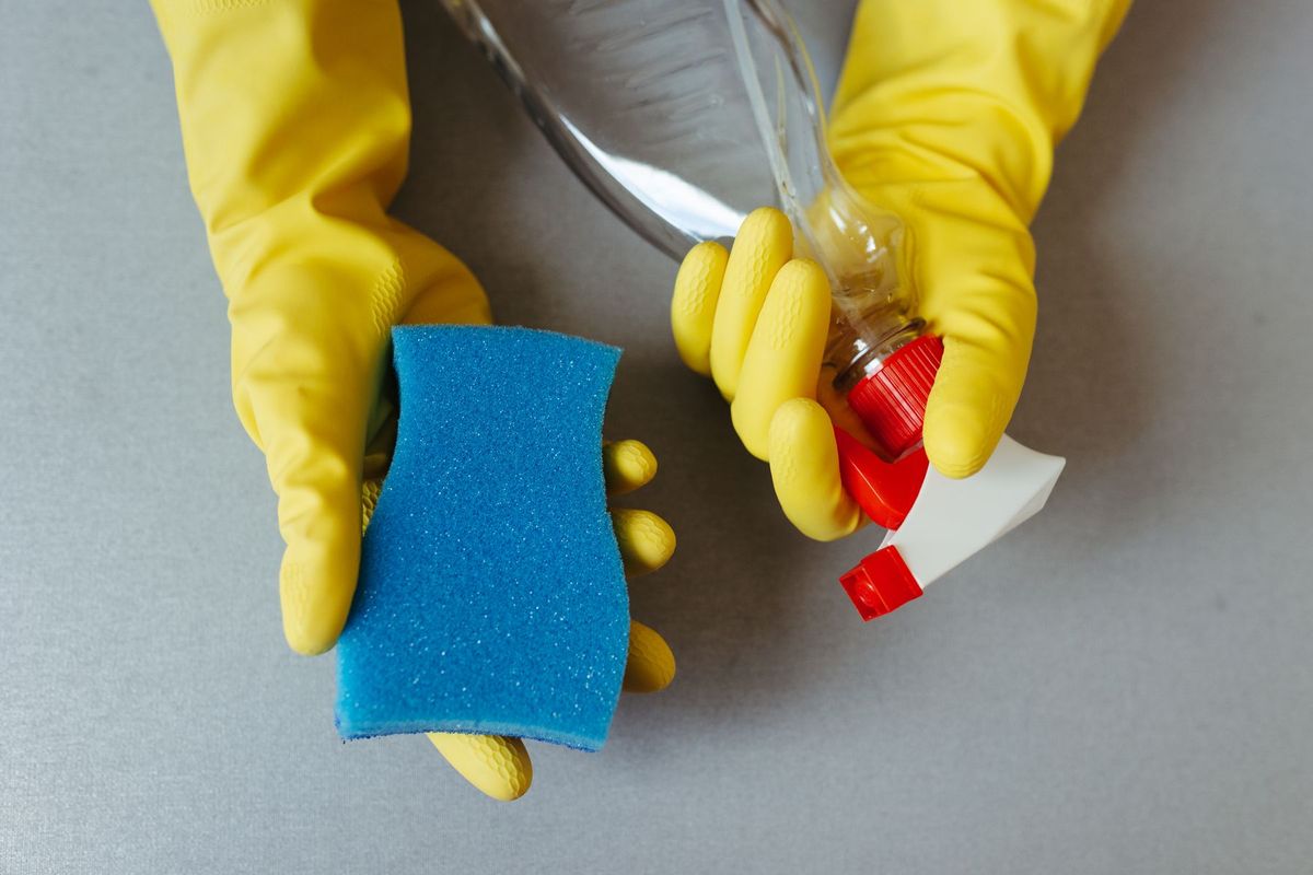 Hands in yellow rubber gloves holding a blue sponge and a spray bottle