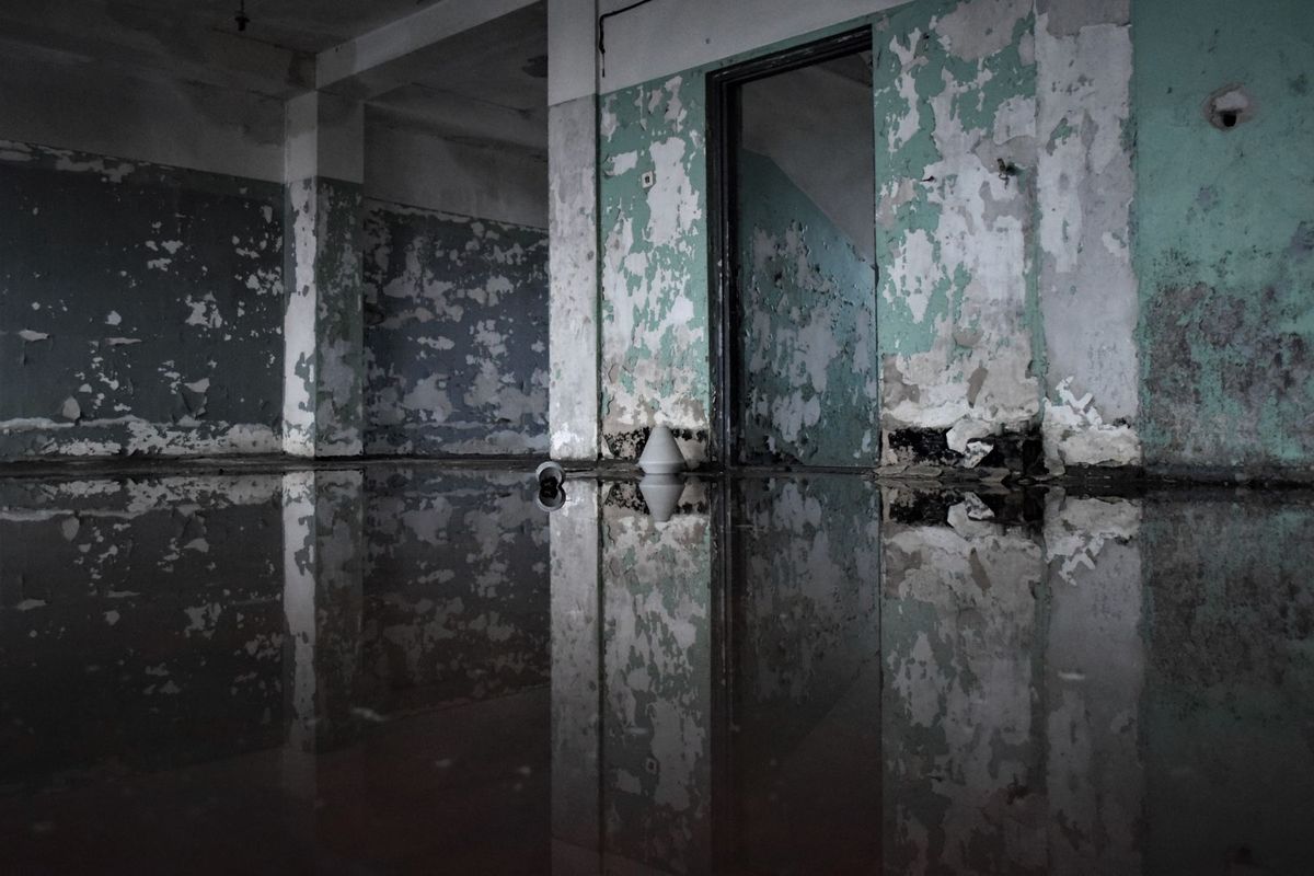 Dark room with standing water across the floor and peeling, water-stained walls