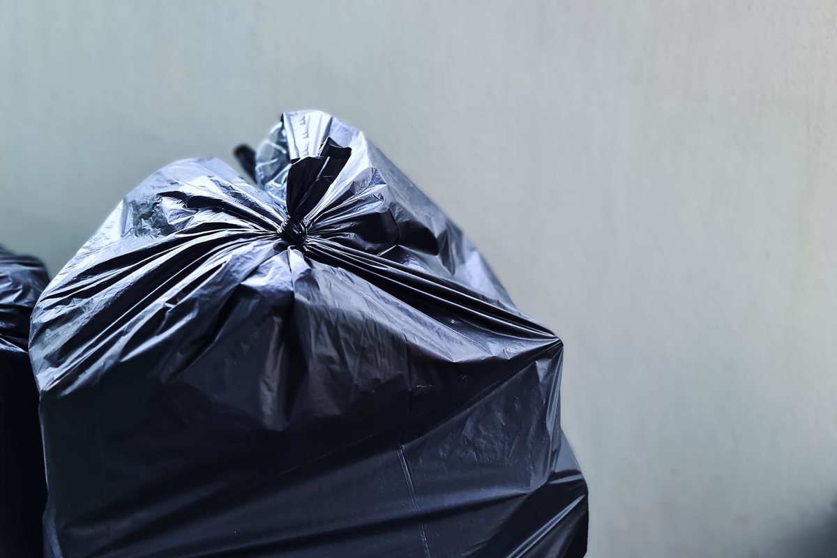 Tied black plastic trash bag against a wall