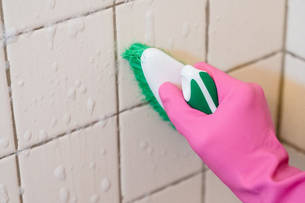 Gloved hand scrubbing a tiled wall with a stiff brush
