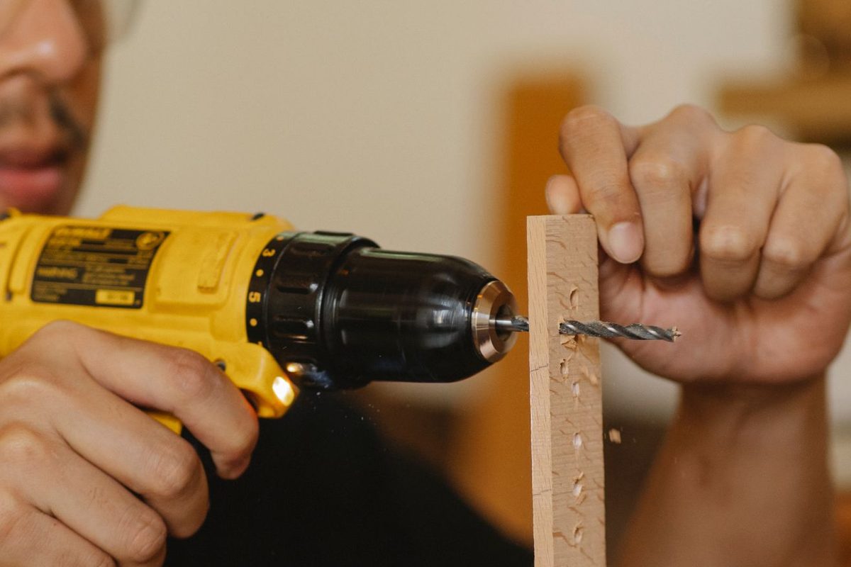 Close-up of hands using a cordless drill to drill a hole in a wooden strip