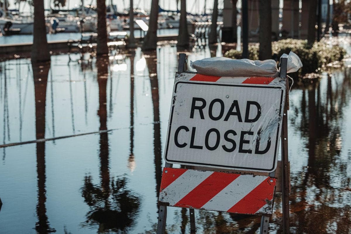 Road closed sign standing in floodwater along a waterfront with palm trees