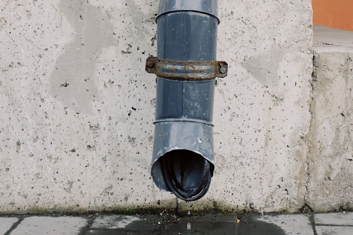 Downspout ending at the base of a wall with water stains on the pavement