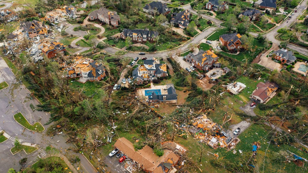 Aerial view of a neighborhood after a windstorm, with damaged roofs, scattered debris and fallen trees
