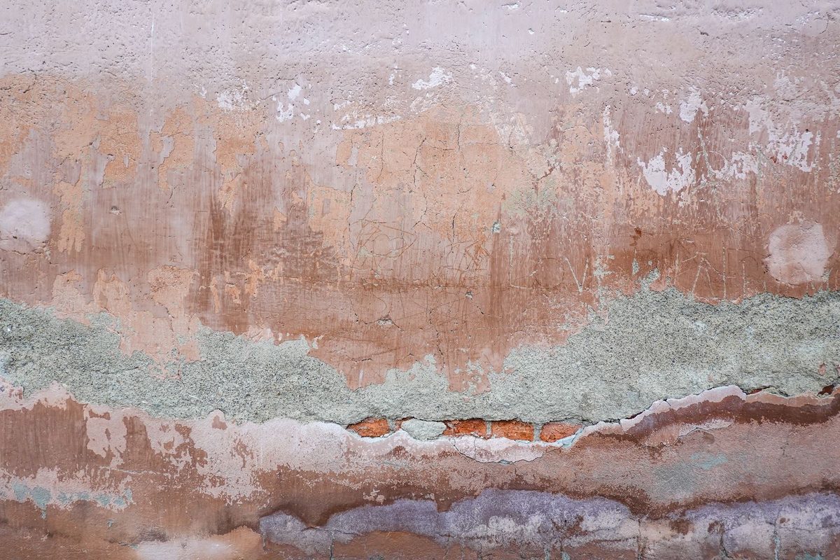 An old plaster wall stained and crumbling along a horizontal band