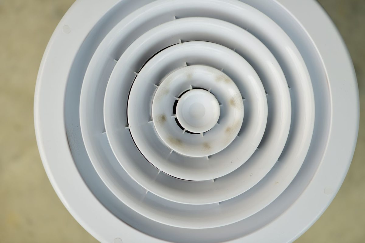 Round white ceiling air vent with dark spots on the louvers