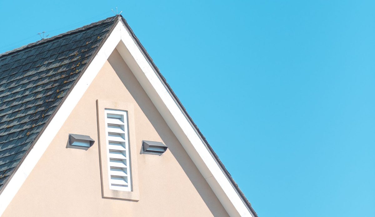 Close view of a gable roof edge with white trim along the rake and a louvered vent in the wall below