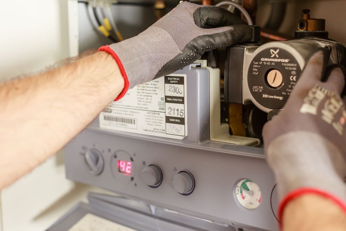 Gloved hands adjusting the pump on a wall-mounted heating unit