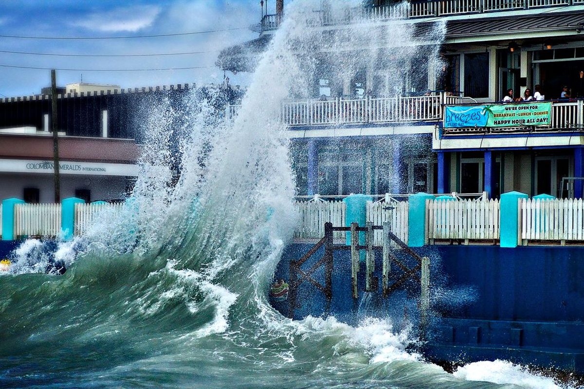A large wave crashing over a seawall in front of a waterfront building