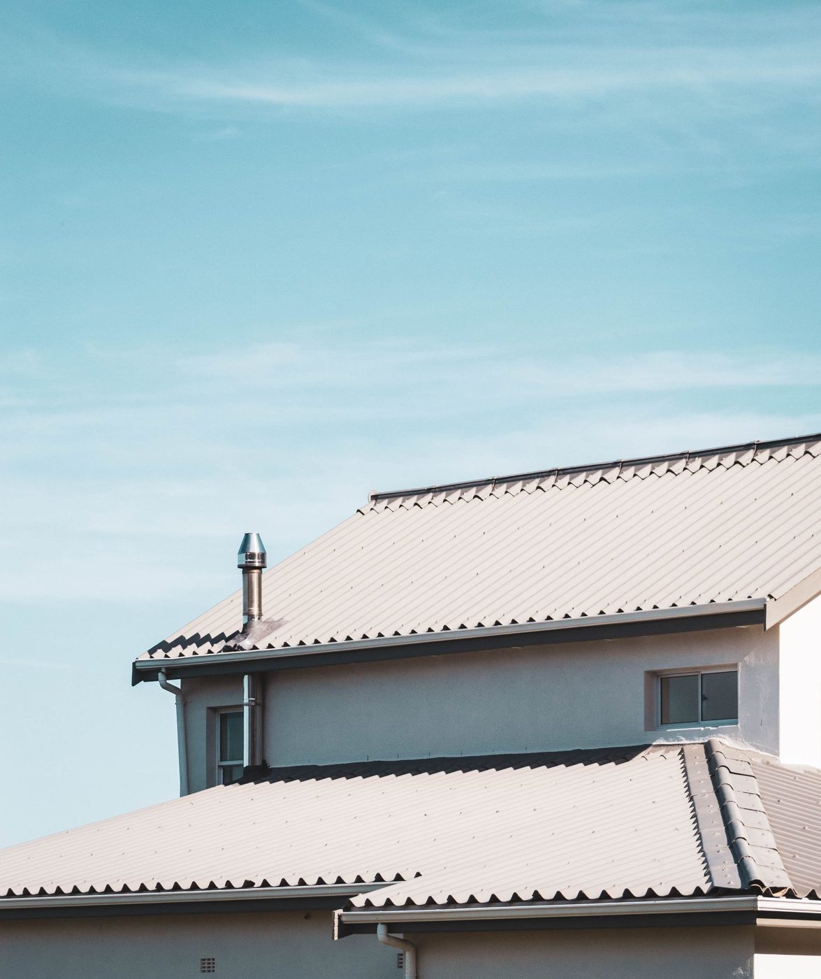Two-story house with low-pitched roofs, showing the overhangs, fascia and gutters along the roof edges against a blue sky