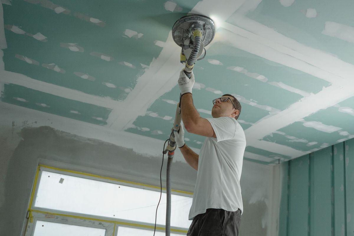 A worker sanding a new drywall ceiling