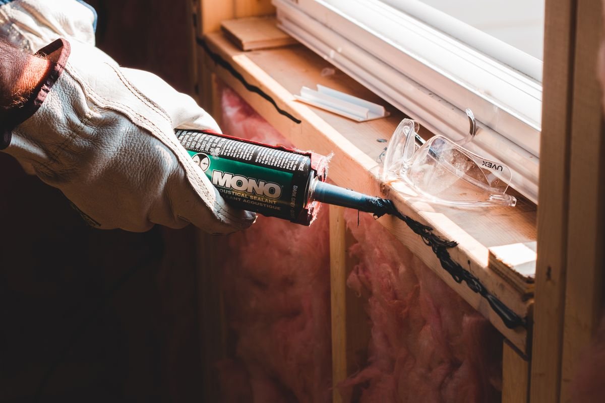 Gloved hand applying sealant along a window frame during installation
